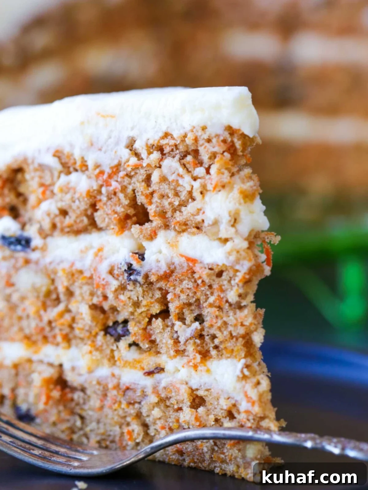 A side view of a beautifully frosted three-layer carrot cake, showcasing its moist texture.