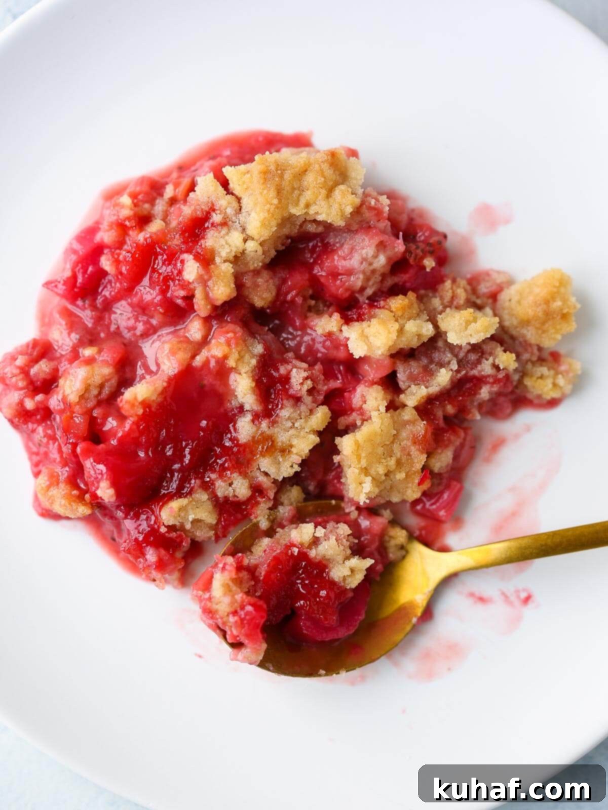 A serving of strawberry rhubarb crumble on a white plate with fruit showing through.