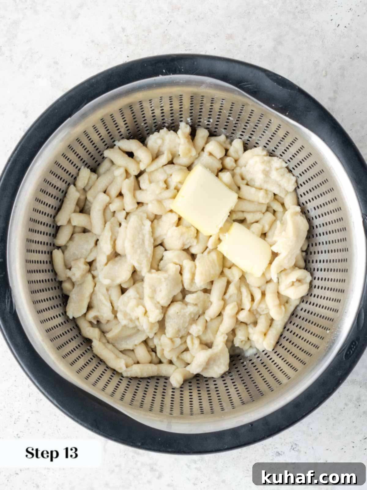 Freshly cooked spaetzle draining in a colander, with a knob of butter added for tossing.