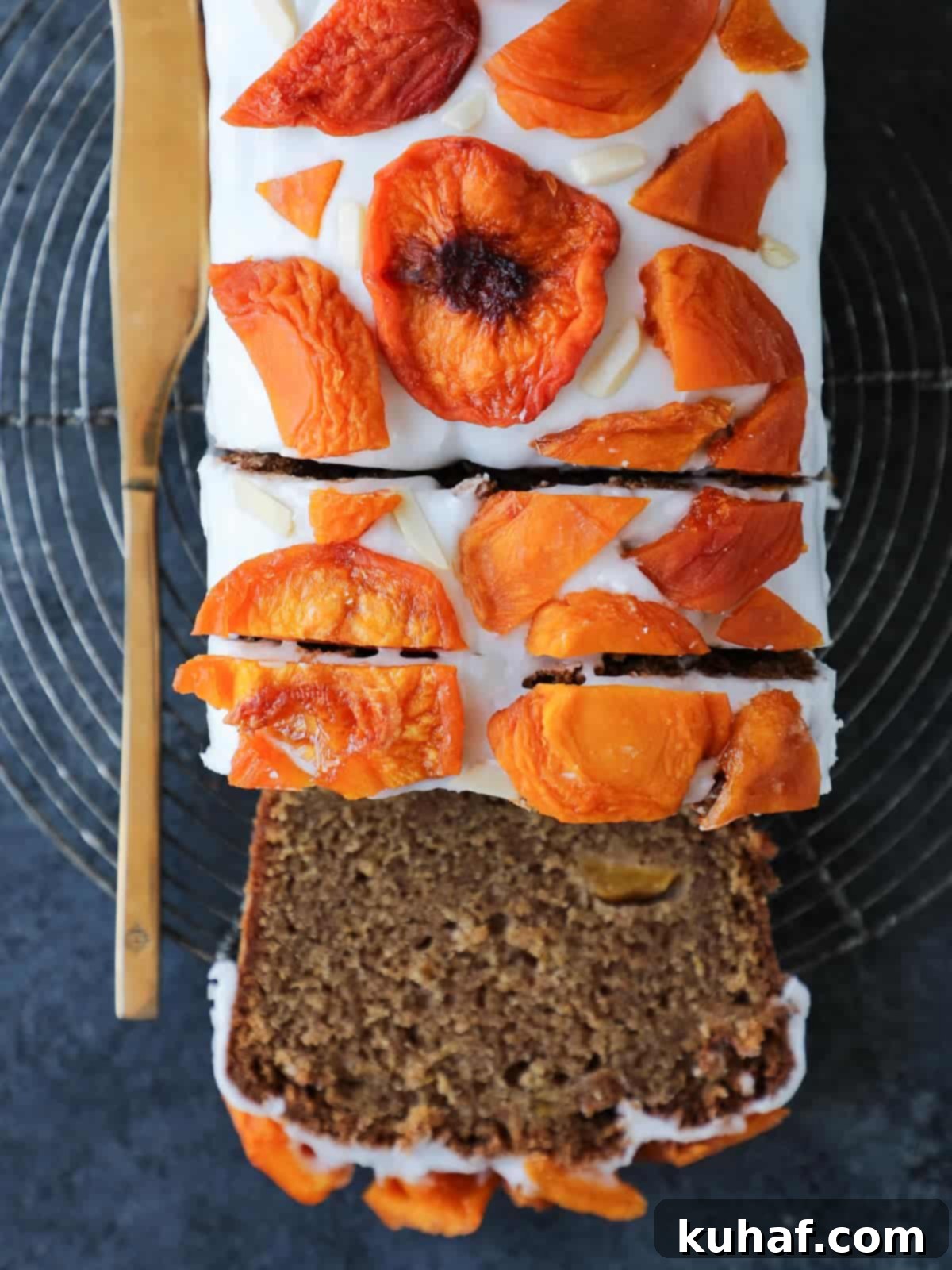 A beautiful loaf of freshly baked peach cake, partially sliced to reveal its moist, tender interior studded with chunks of ripe peaches.