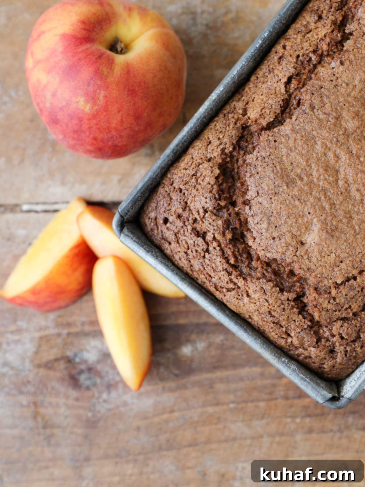 A freshly baked, golden brown peach loaf cake, unglazed, resting in its pan to cool before being moved to a wire rack.