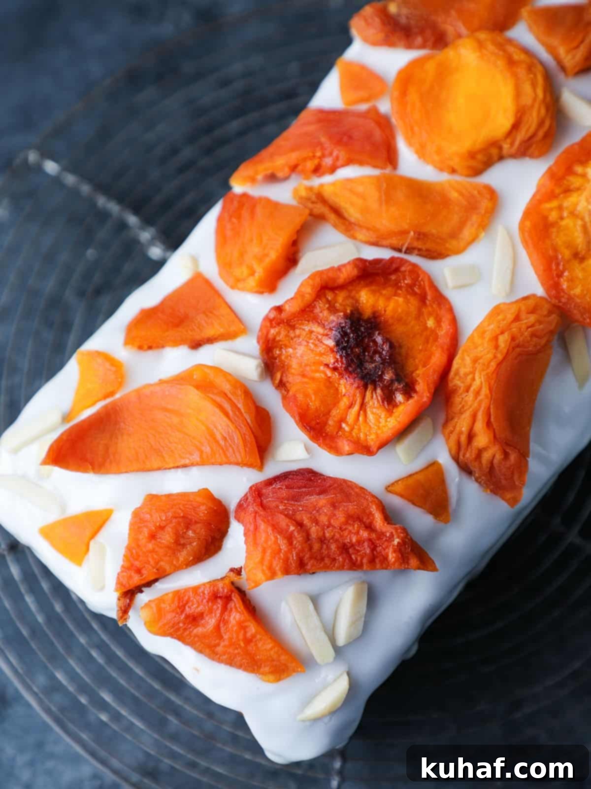 A beautifully glazed peach cake, artfully topped with dried peach slices and delicate slivered almonds, resting on a cooling rack, ready to be served.