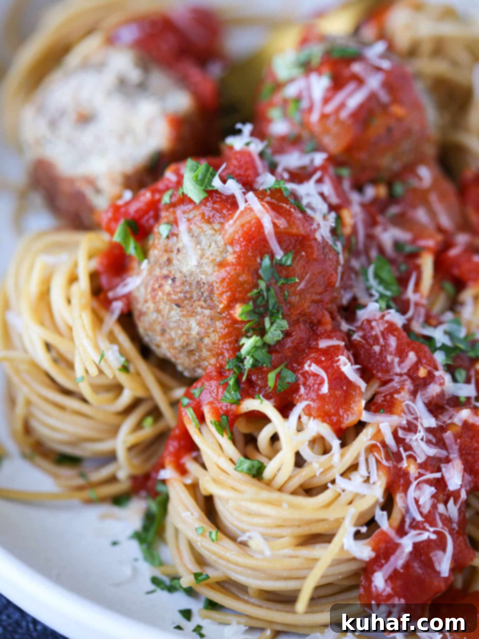 Baked turkey meatballs in a bowl of spaghetti, garnished with fresh herbs.