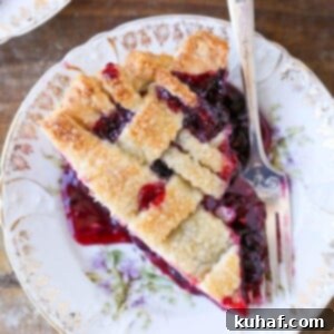 A serving of mixed berry pie with a lattice top and silver fork.