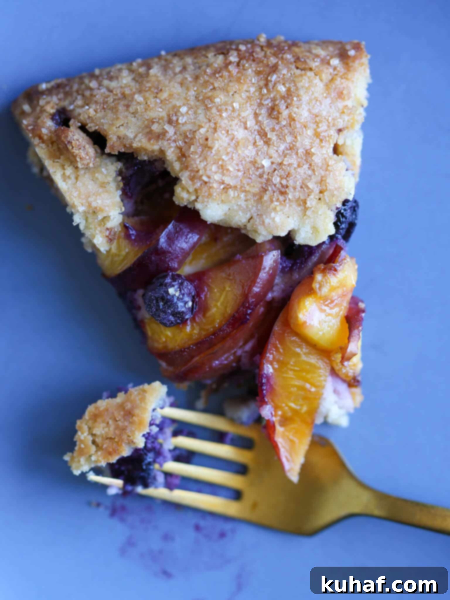 A close-up of a slice of Blueberry Nectarine Galette, showing the flaky crust and fruit, with a gold fork.