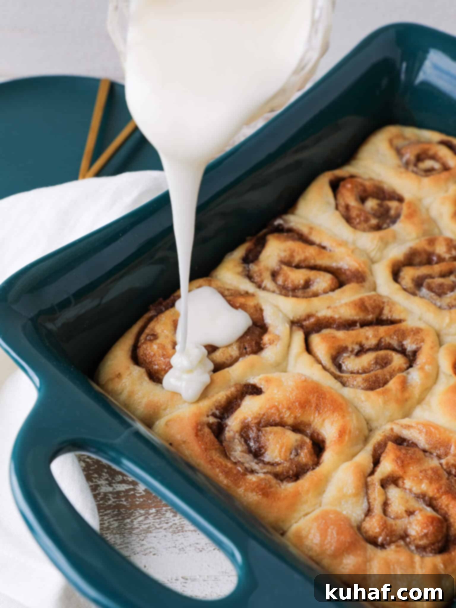 The Best Cinnamon Rolls glazing the baking dish, golden brown and covered in cream cheese frosting.