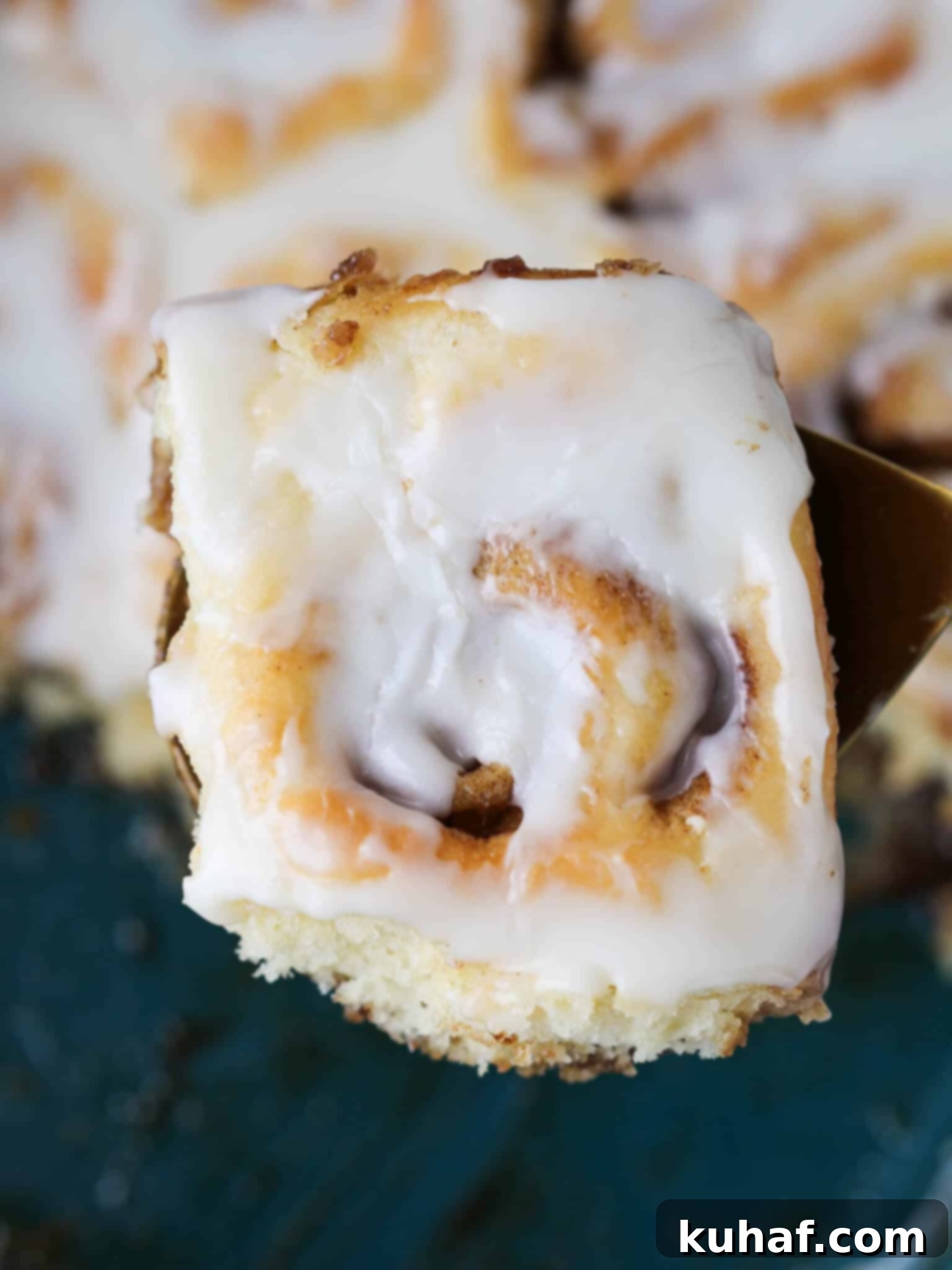 The Best Cinnamon Rolls top view roll on gold server, showcasing a beautifully swirled center and generous frosting.