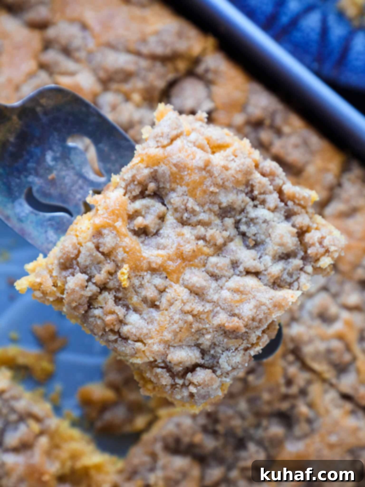 A large slice of pumpkin coffee cake being lifted from the baking dish with a server, showcasing the layers of cake and streusel.