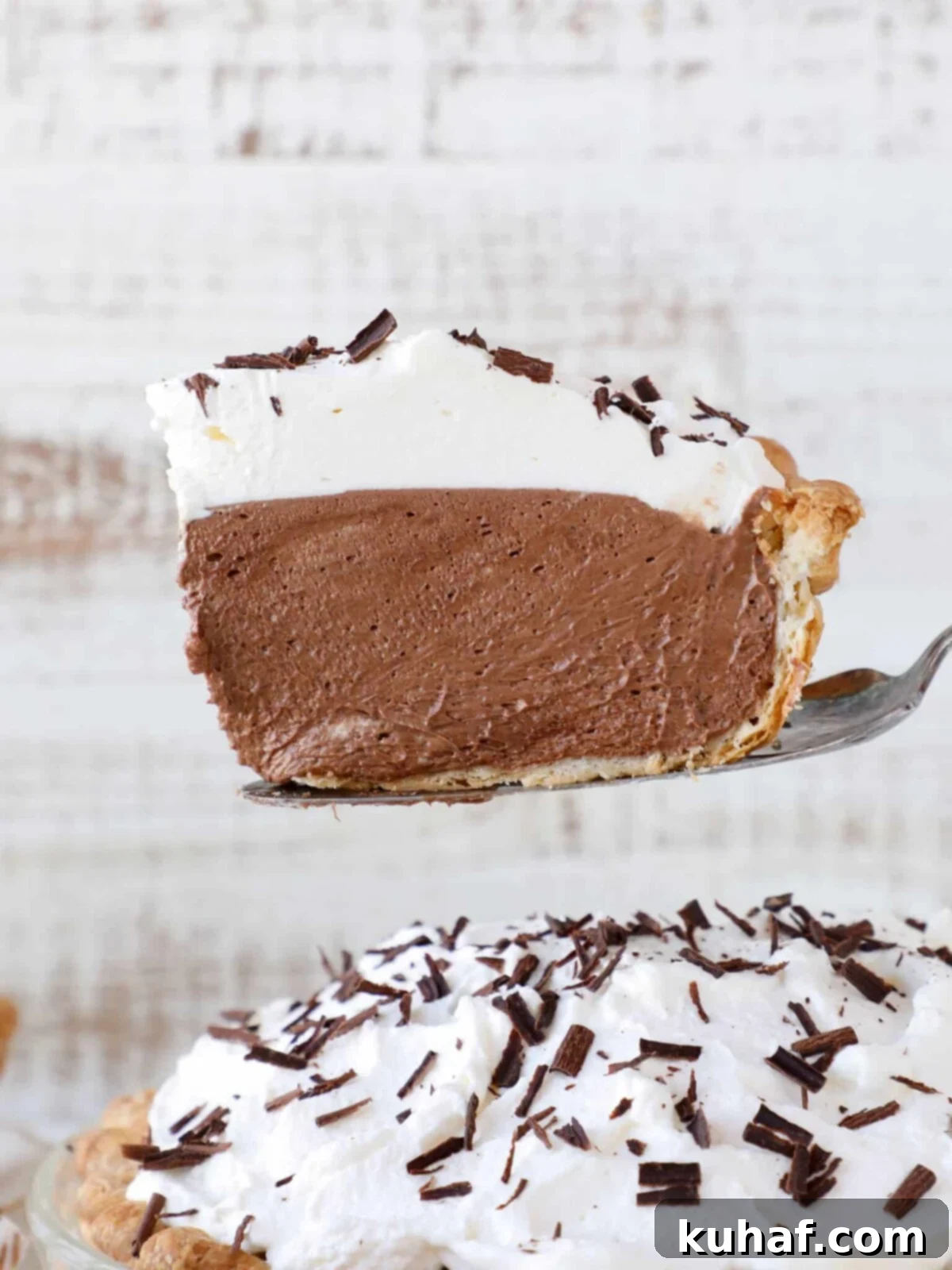 A perfectly sliced French Silk Pie, showcasing its flaky crust, rich chocolate filling, and generous whipped cream topping, ready to be served.