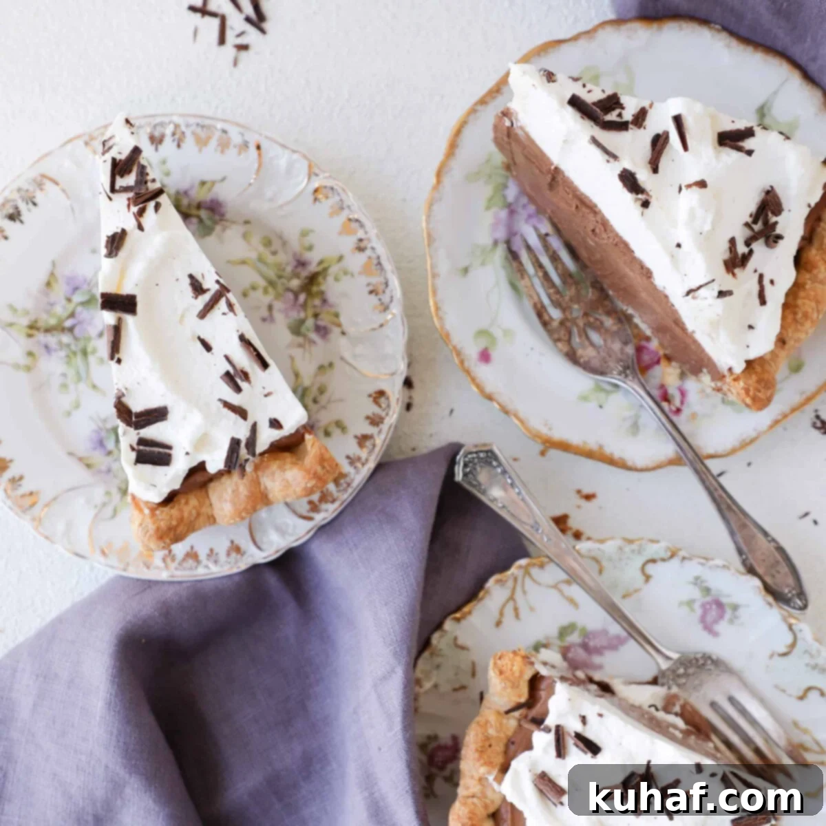 Three slices of French Silk Pie artfully arranged on white plates, highlighting the distinct layers of crust, chocolate, and whipped cream.