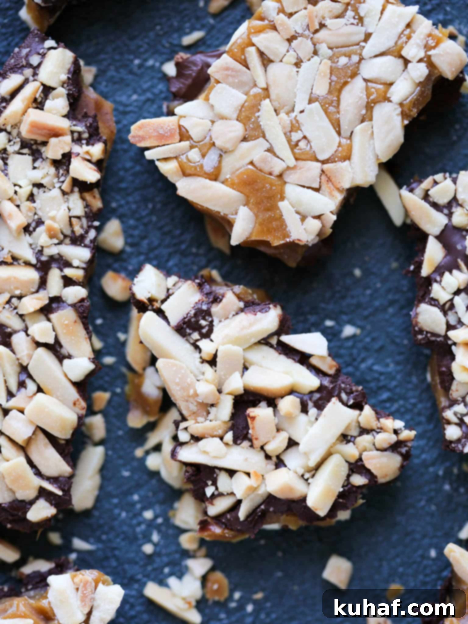 Broken pieces of homemade chocolate almond toffee on a white surface