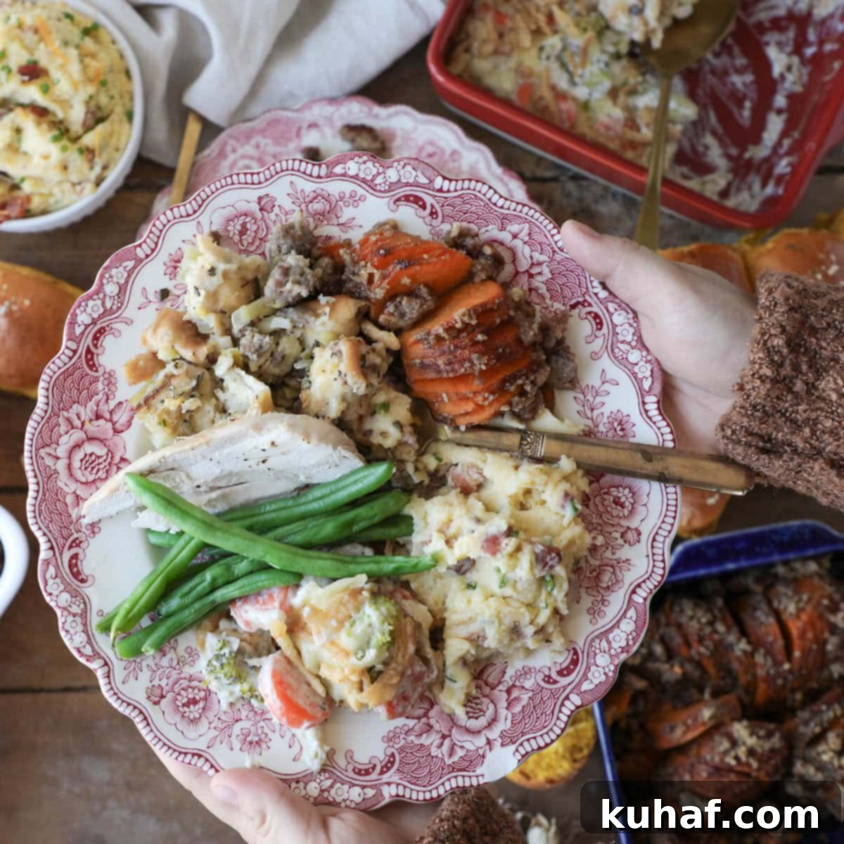A hand holding a plate piled high with a variety of delicious Thanksgiving side dishes.