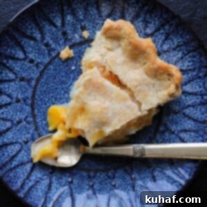 A delectable slice of Old Fashioned Peach Pie, elegantly presented with a vintage gold fork, highlighting its tender filling and inviting texture.