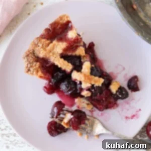A close-up of a slice of Cherry Pie Almond Crust, showcasing its vibrant red filling and intricate lattice top, a testament to its homemade perfection.