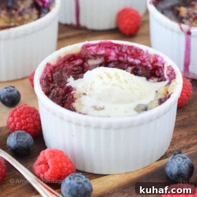 Close-up of a golden brown individual blueberry raspberry crumble in a ramekin, topped with ice cream.