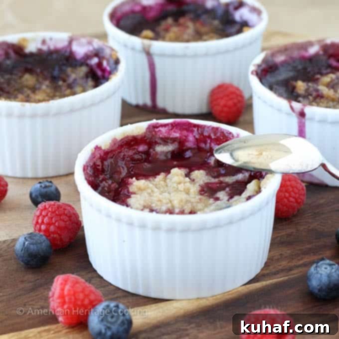 Six individual blueberry raspberry crumbles baking in ramekins on a sheet pan, showing the baking process.