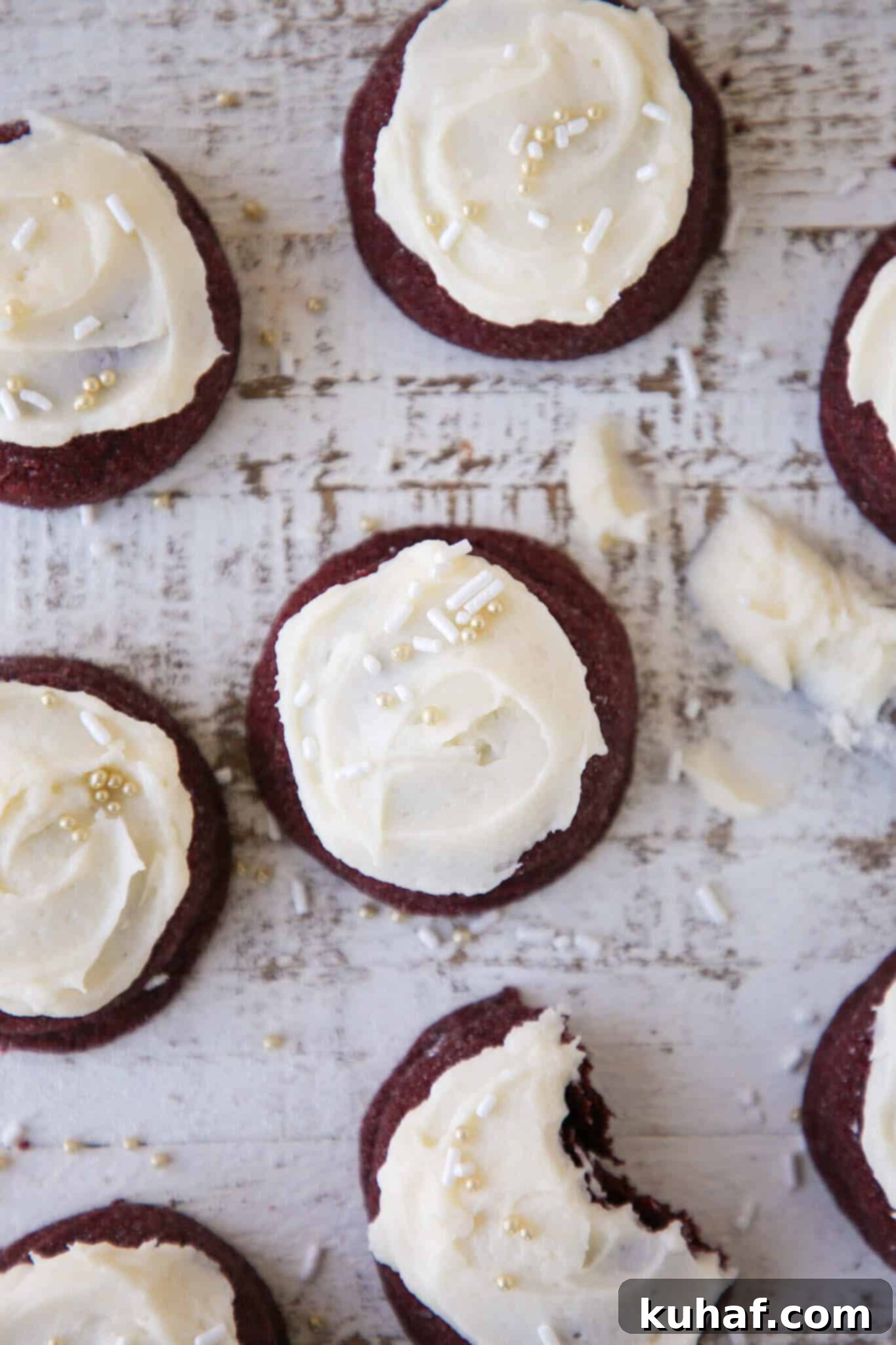 Several red velvet cookies with cream cheese frosting arranged beautifully on a light beige backdrop, showcasing their vibrant color and texture.