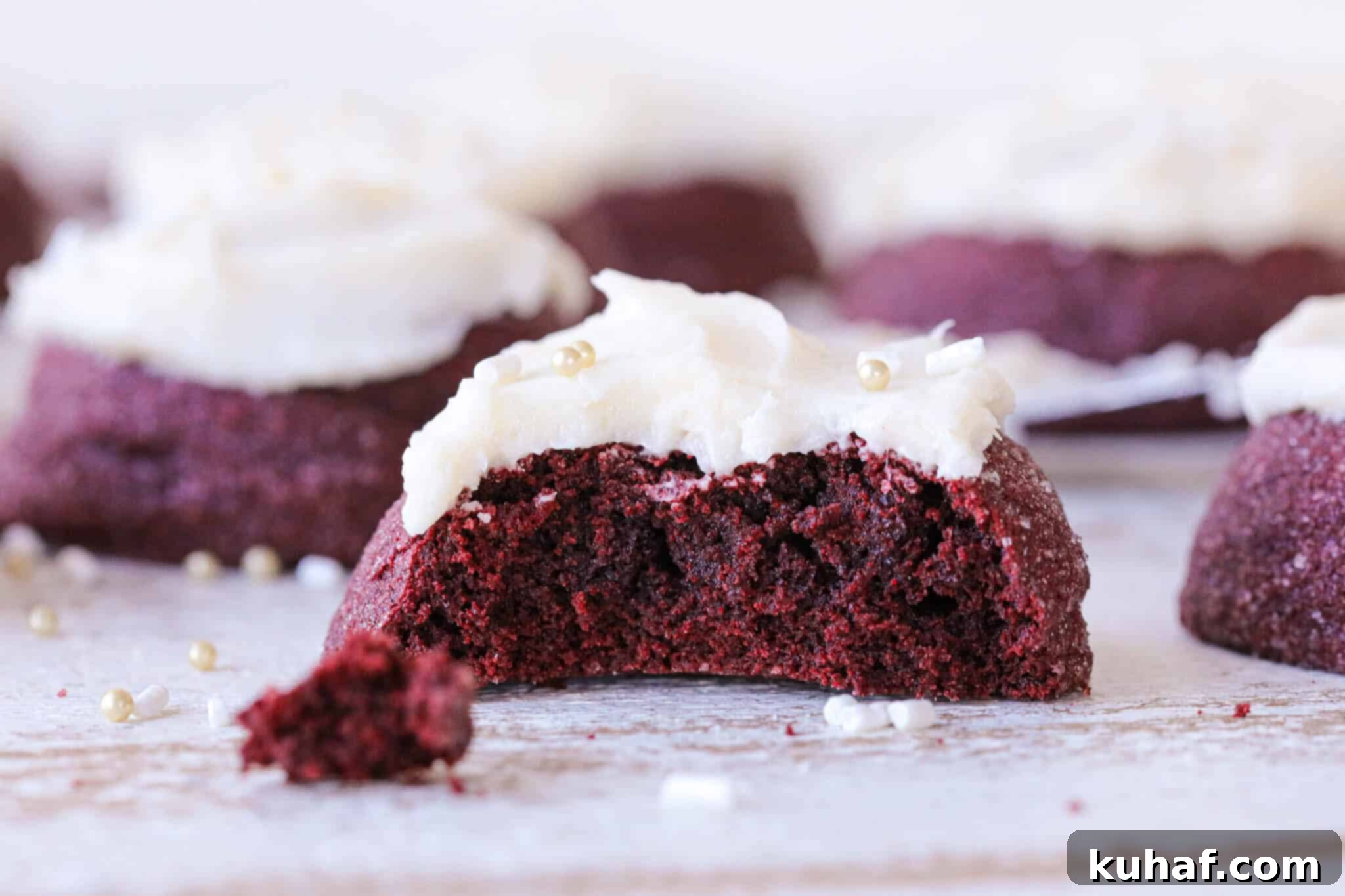 A close-up view of a red velvet cookie's interior crumb, showing its soft, moist texture, with white cream cheese frosting visible on top.