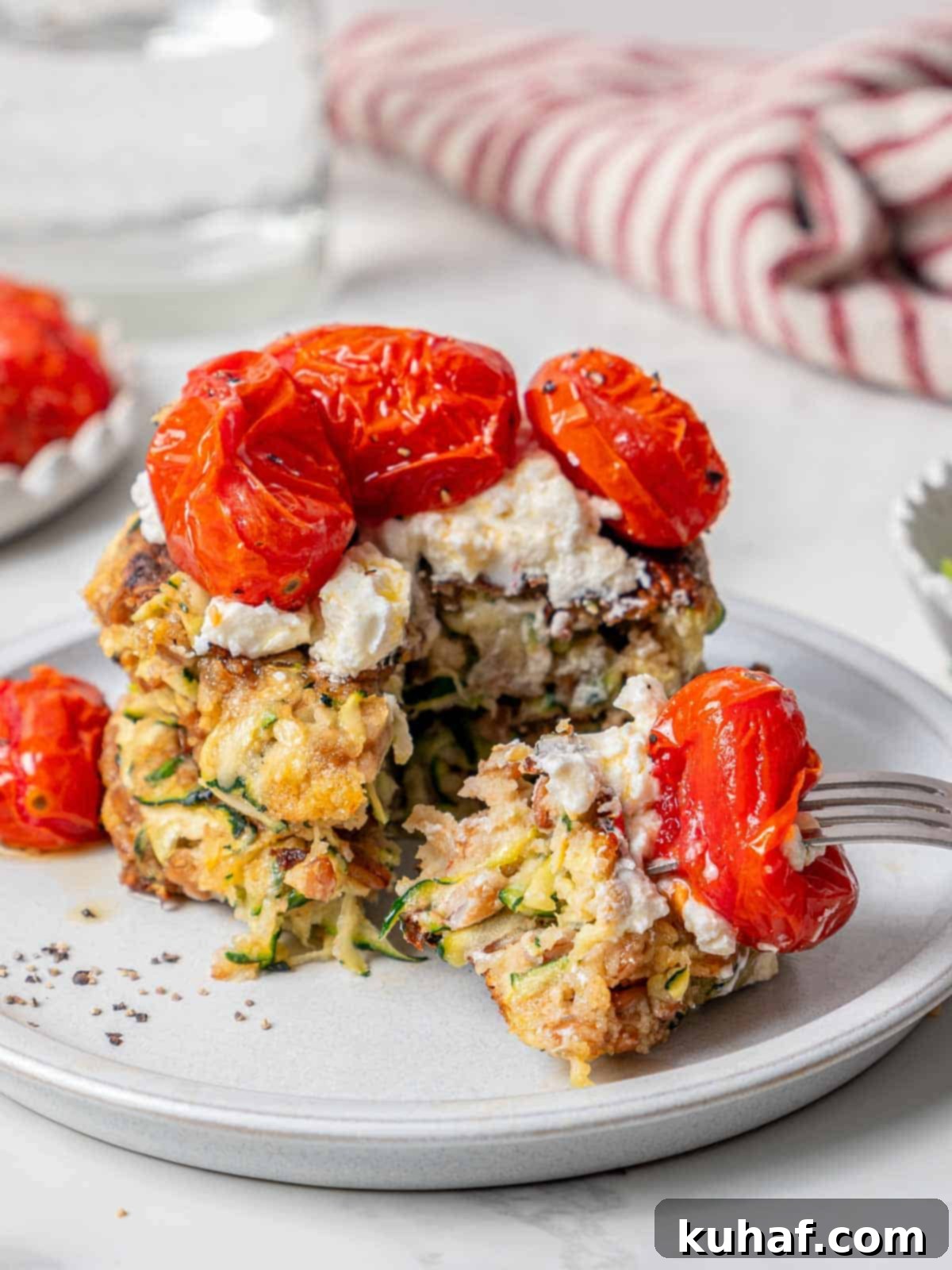 Close-up of a bite of crispy zucchini fritter with goat cheese and tomato on a fork, showing its tender interior and golden exterior.