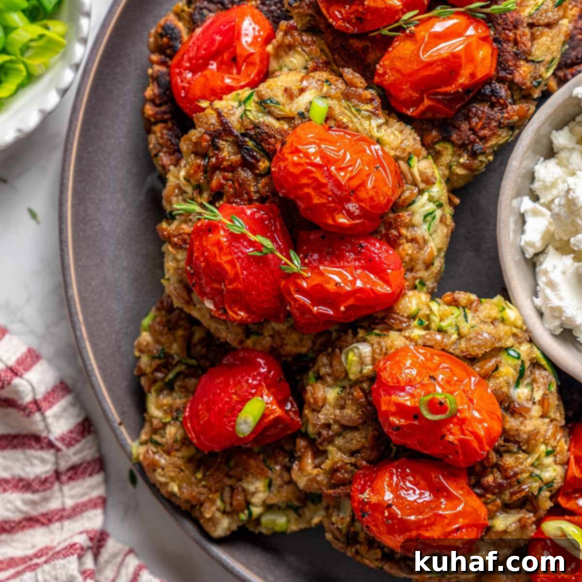 Platter of golden-brown zucchini fritters, perfectly cooked and ready to serve, accompanied by sweet slow-roasted tomatoes, highlighting their irresistible appeal.