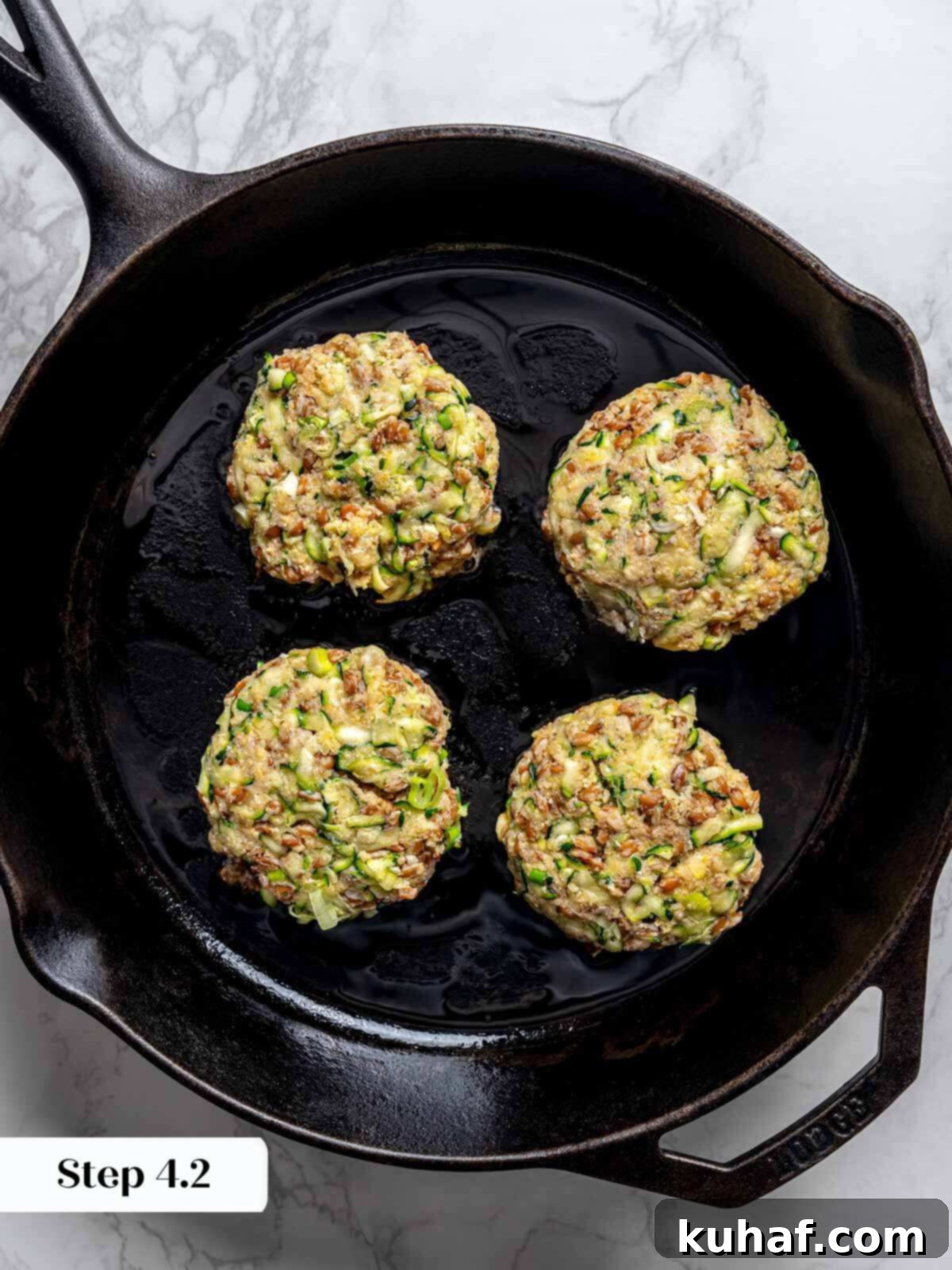 Four perfectly formed, uncooked zucchini fritter patties nestled in a cast iron pan, glistening with oil, ready to be cooked to golden perfection.