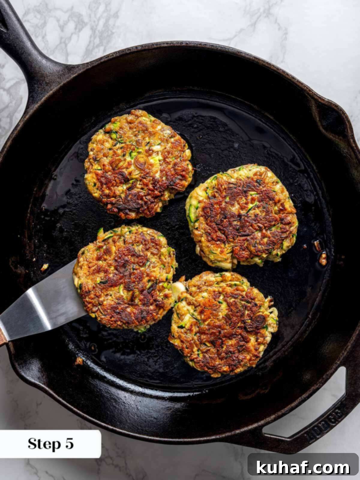 Four golden-brown zucchini fritter patties, beautifully cooked to crispy perfection, resting in a cast iron pan, still warm from the stove.