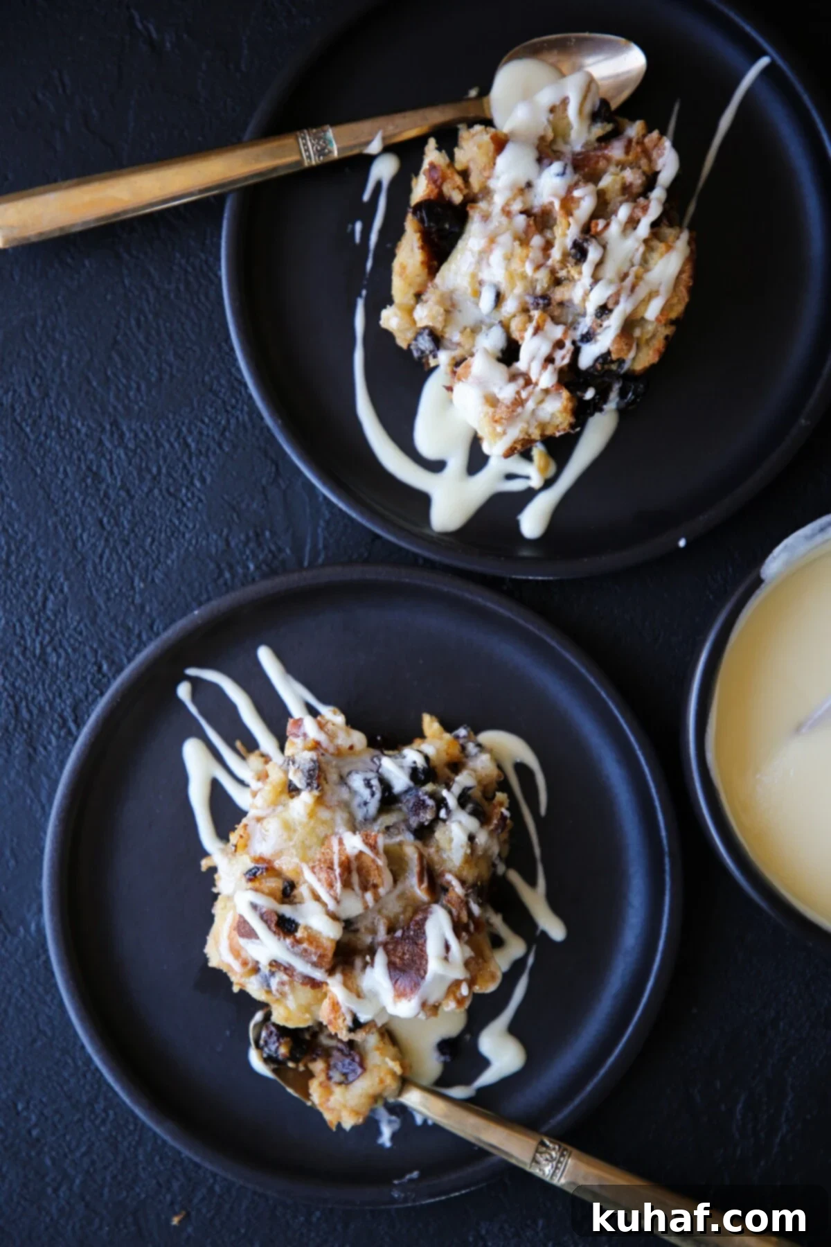 Two servings of bread pudding on black plates, elegantly drizzled with hard sauce, ready to be served.