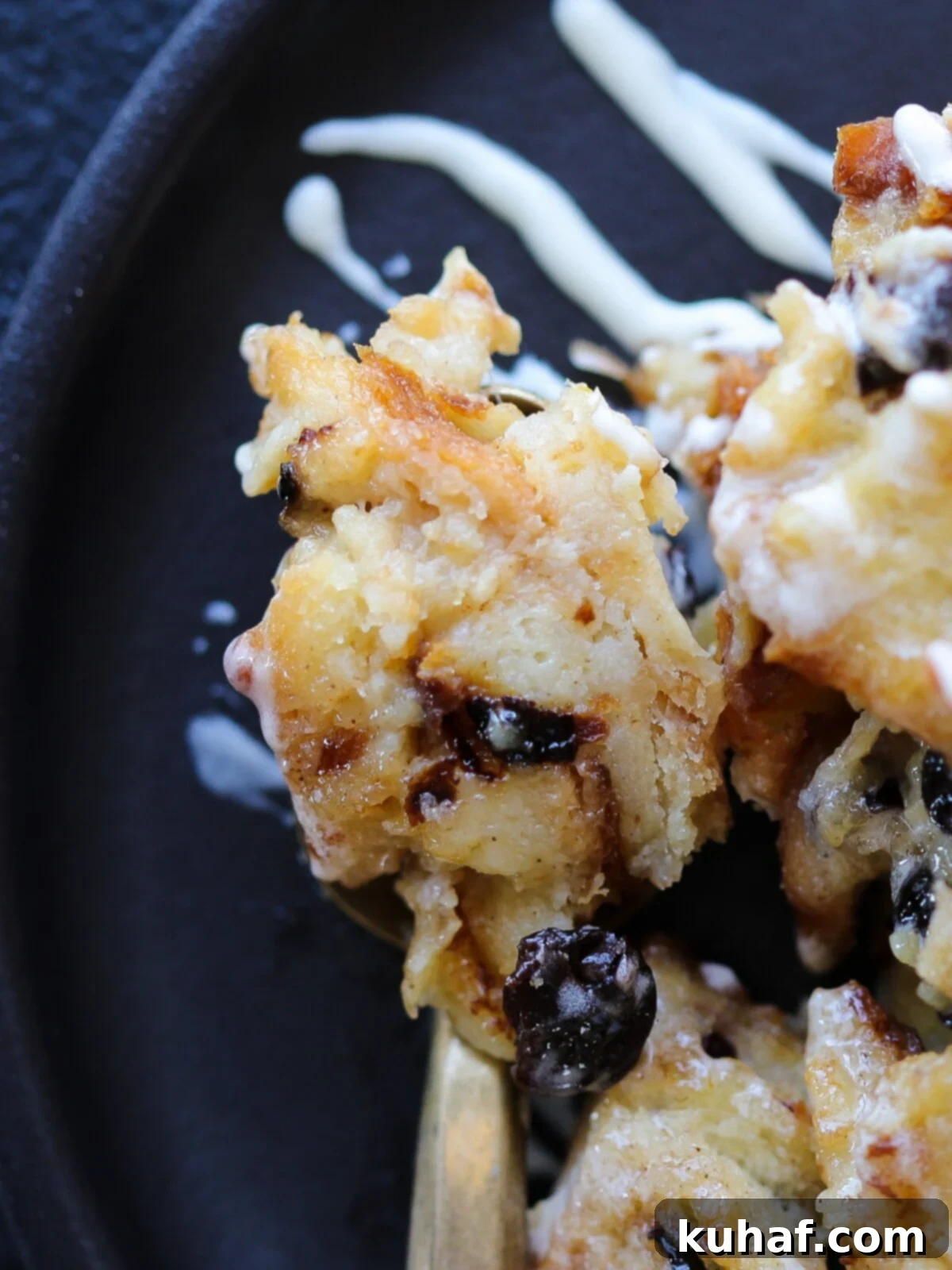 Close-up of a bite of bread pudding on a fork, showcasing its soft, custardy texture and crunchy top.