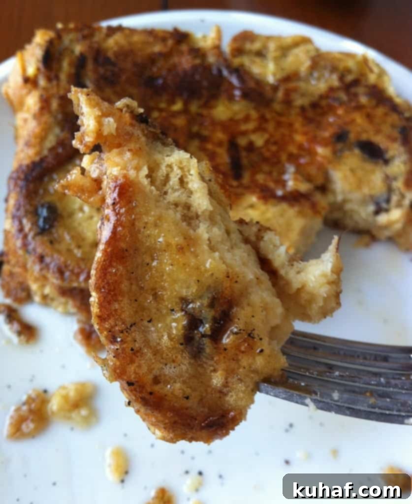 Decadent Cinnamon Raisin French Toast 6 A fork taking a bite of Cinnamon Raisin French Toast, showing its soft interior