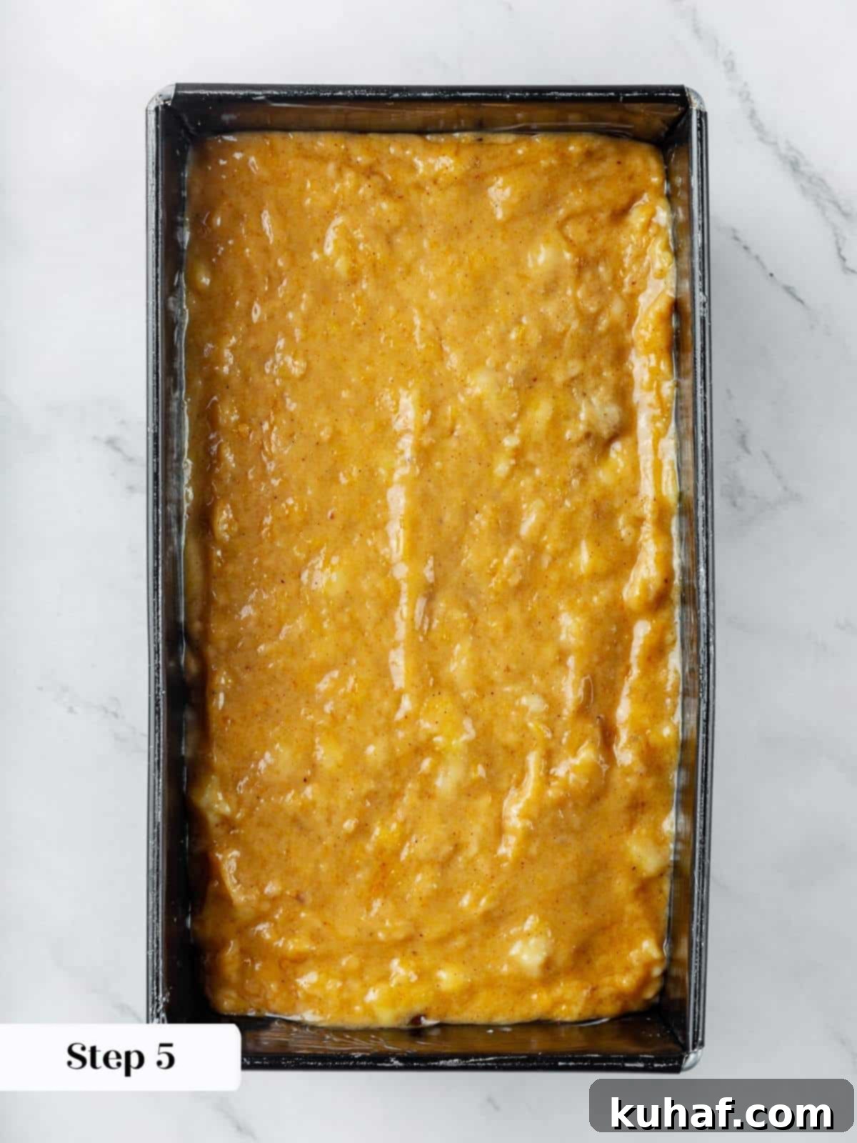 Unbaked pumpkin banana bread batter spread evenly and smoothly in a loaf pan, perfectly prepared and ready for baking, showcasing its rich, warm color.