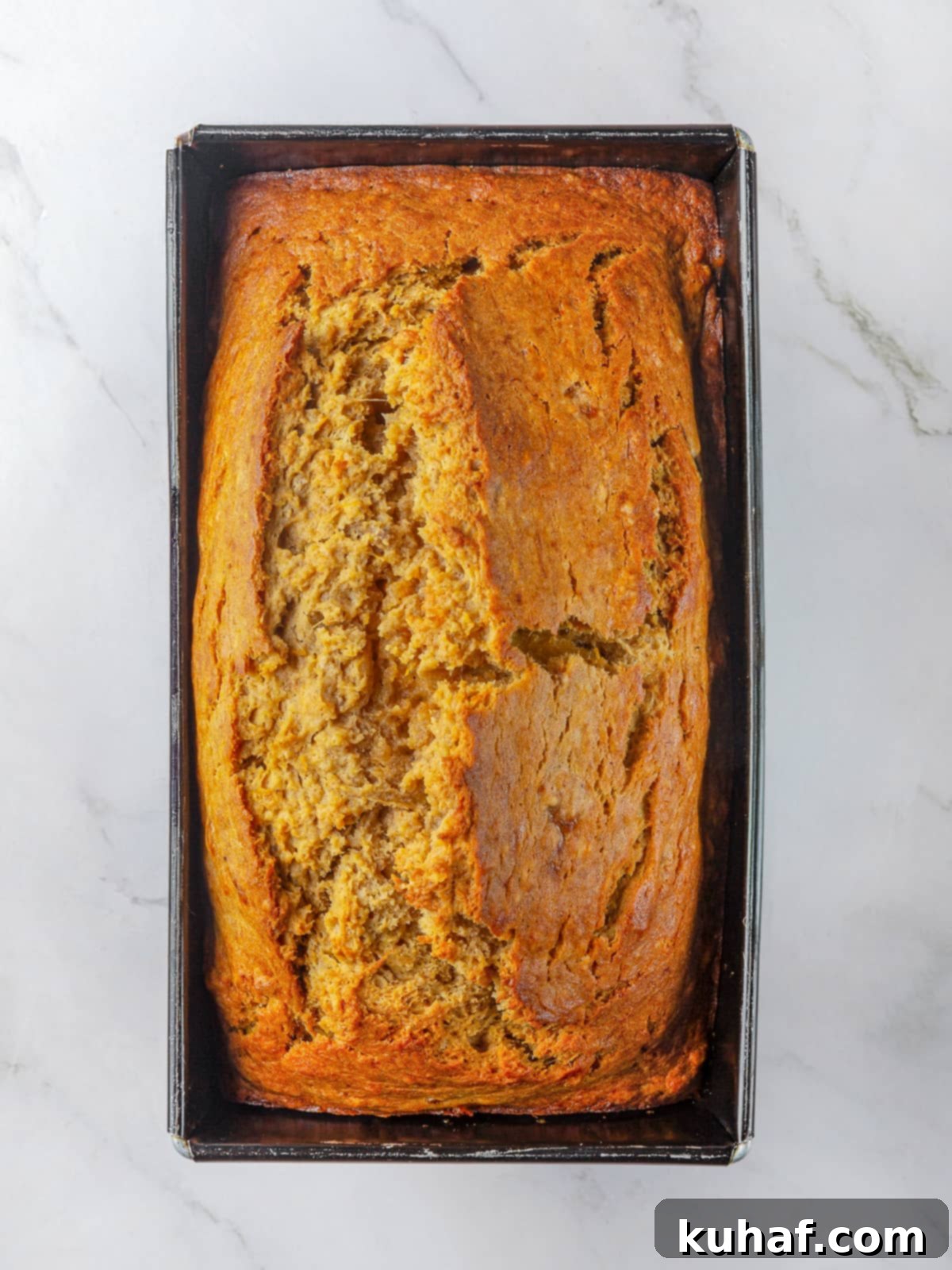 A beautifully baked pumpkin banana bread, fresh from the oven, with a distinct, crackled golden-brown top crust, indicating perfect doneness and a delicious, spiced aroma.