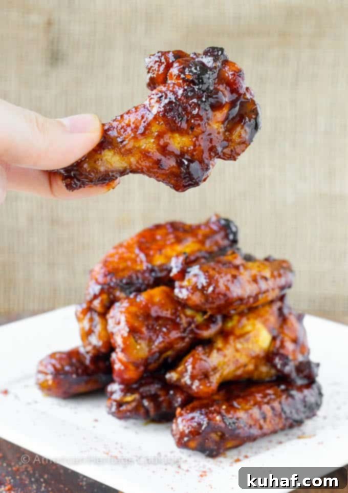 A stack of baked chicken wings with one wing being held up, glistening with sweet and spicy chipotle maple sauce.