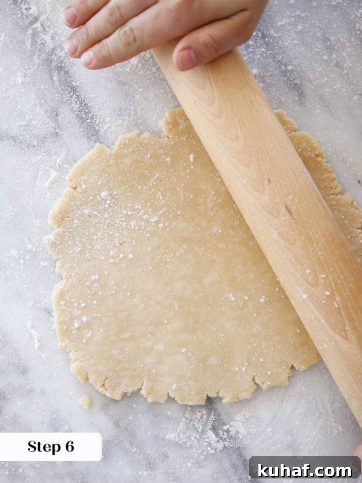 Rolling Crisco pie dough with a wooden rolling pin on a marble surface.
