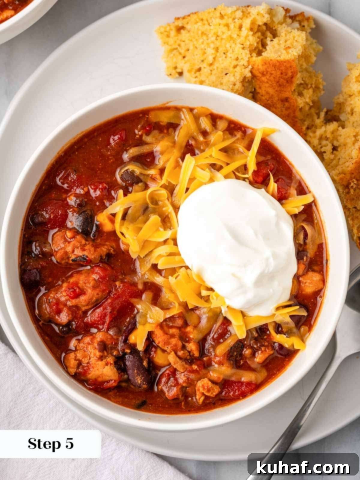 Smoky Chipotle Heat 9 A bowl of chipotle chili topped with cool sour cream and shredded cheddar cheese, ready to be enjoyed.