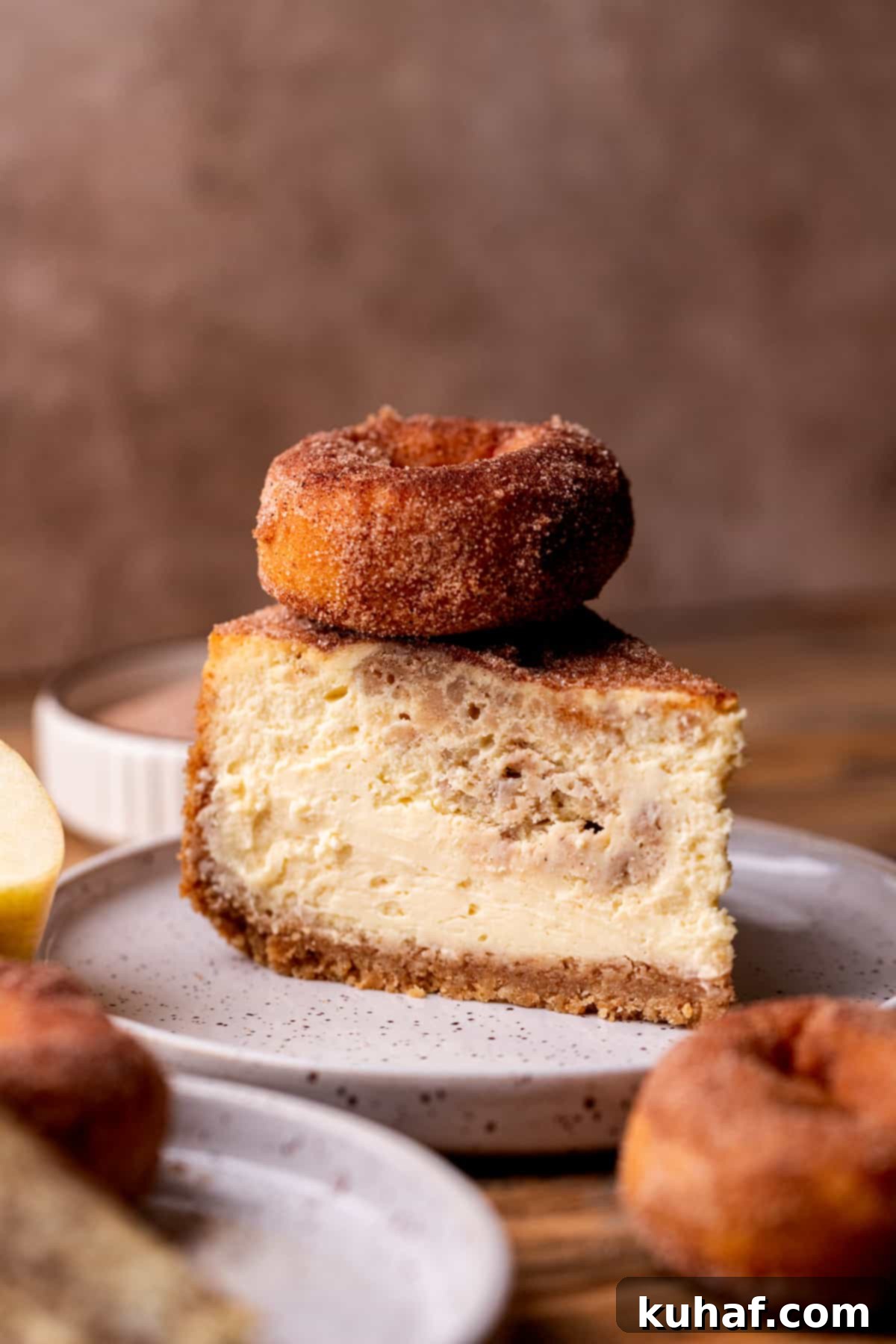 A rich slice of apple cider cheesecake, topped with a mini donut, showcasing its creamy texture and streusel.