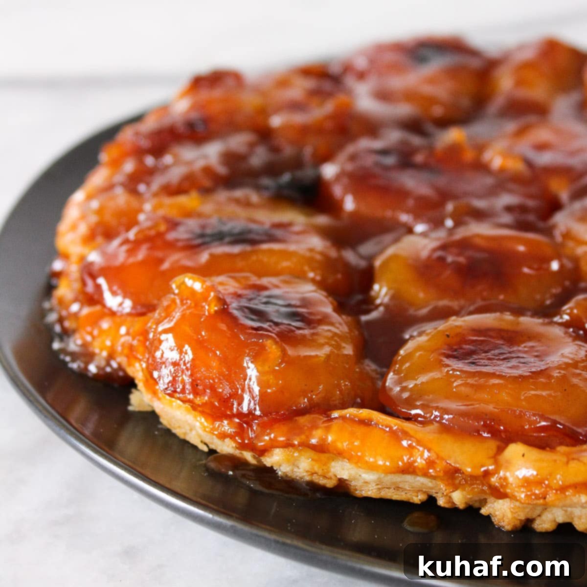 Exquisite Apple Tarte Tatin, golden caramelized apples under flaky pastry, on a black plate.