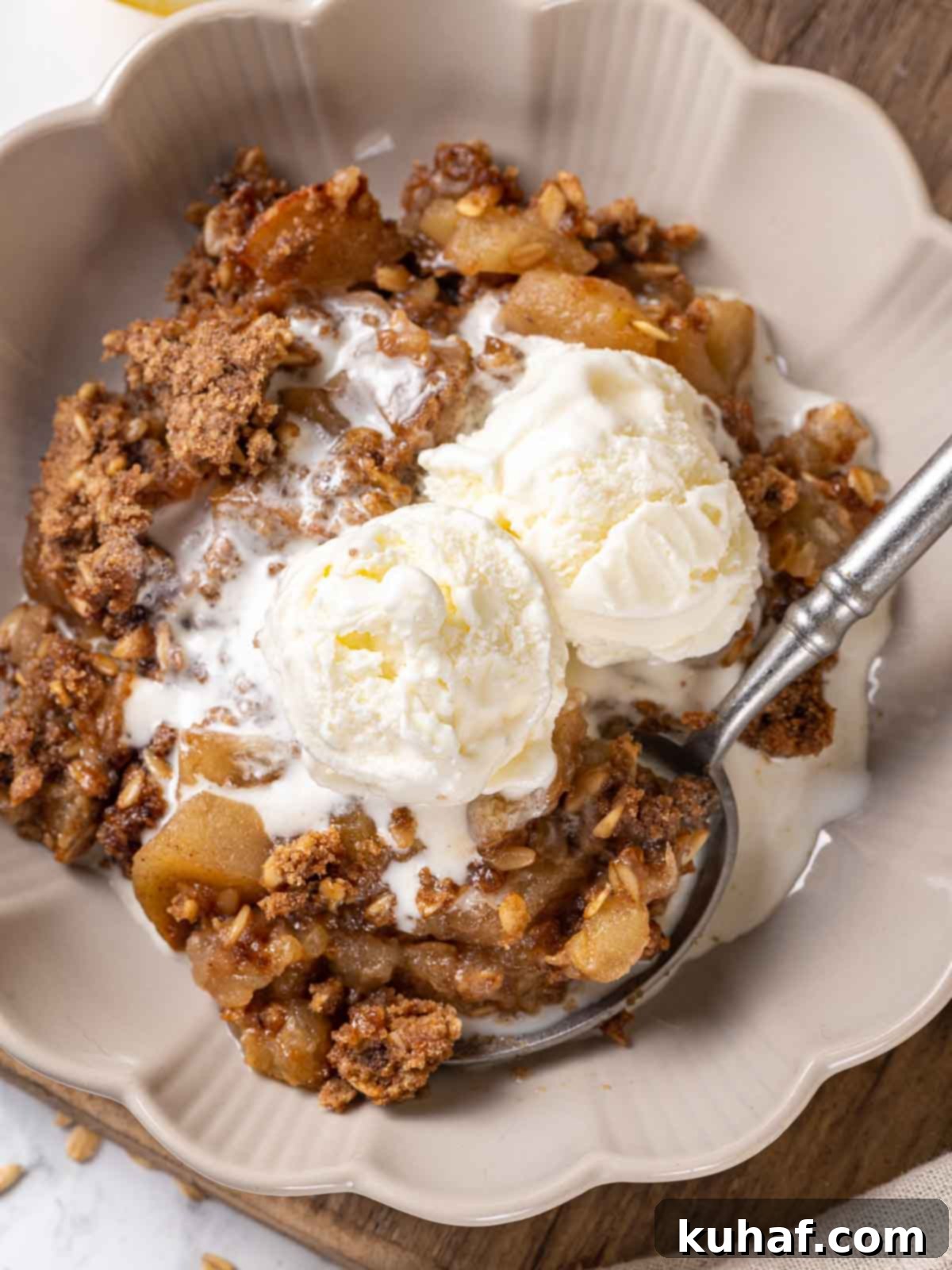 A comforting bowl of easy apple crisp, topped with melting vanilla ice cream and served with a pewter spoon.