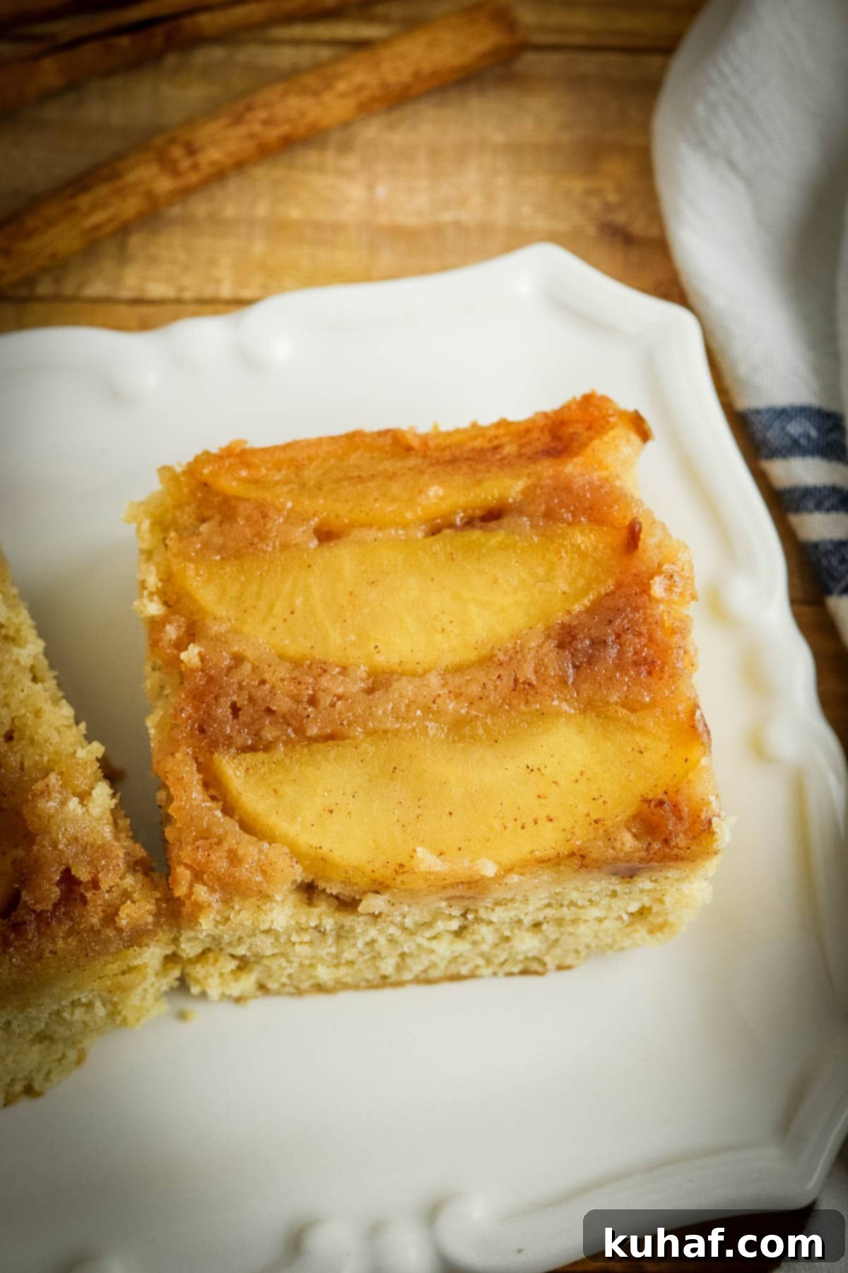 A perfect slice of apple upside-down cake, glistening with caramel apples, served on a elegant white cake plate.