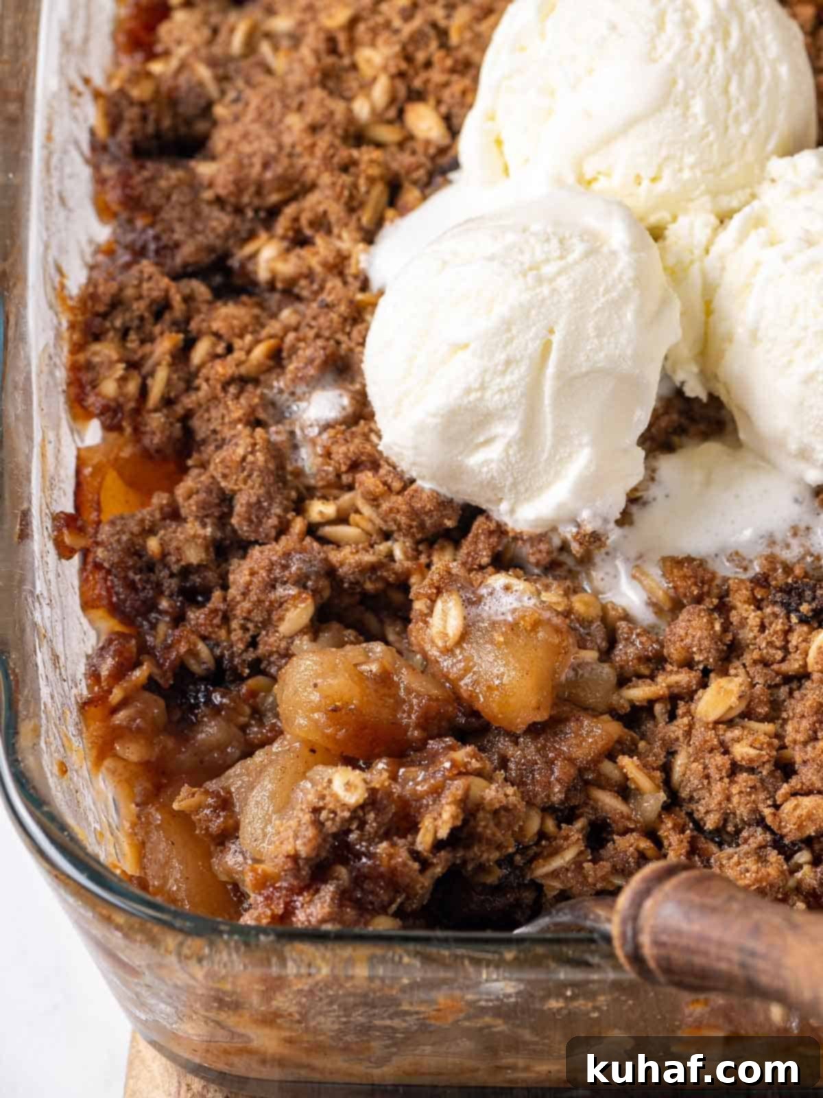 Warm apple crisp in a baking dish, generously topped with melting vanilla ice cream, ready to be served.