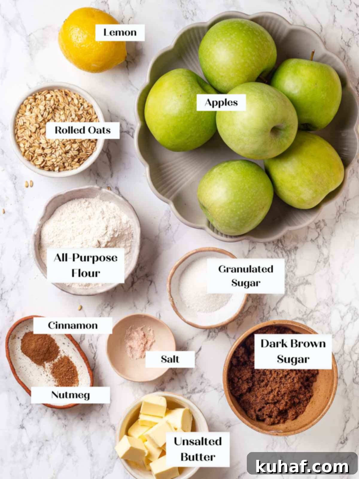 Array of fresh ingredients for apple crisp displayed on a marble countertop, including apples, cinnamon, oats, and butter.