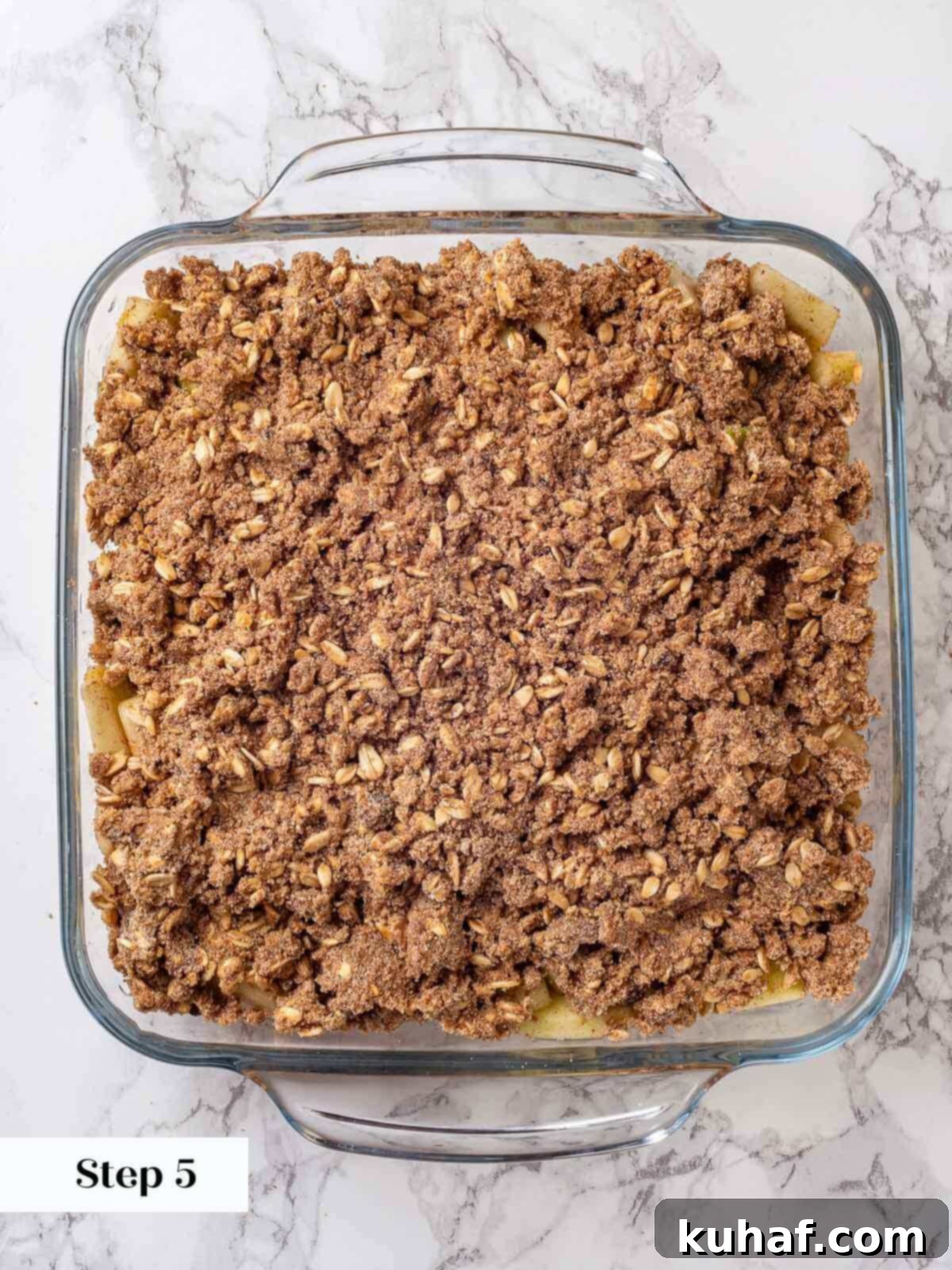 Unbaked apple crisp in a square baking dish, showing the layer of apples covered with crumbly oat topping.