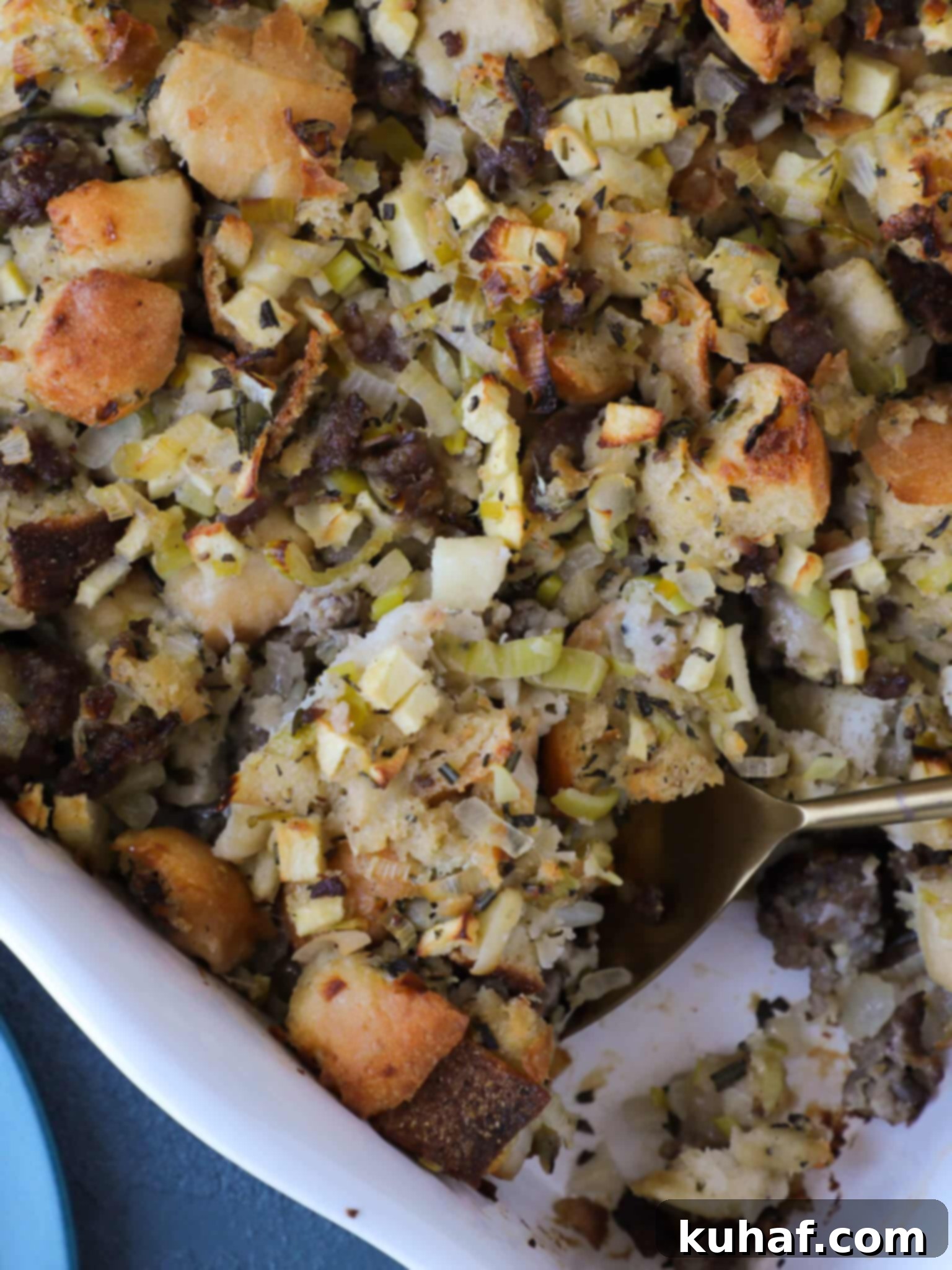 Apple Sage Sausage Stuffing in a white baking dish with a spoon, highlighting its golden crust and moist interior.