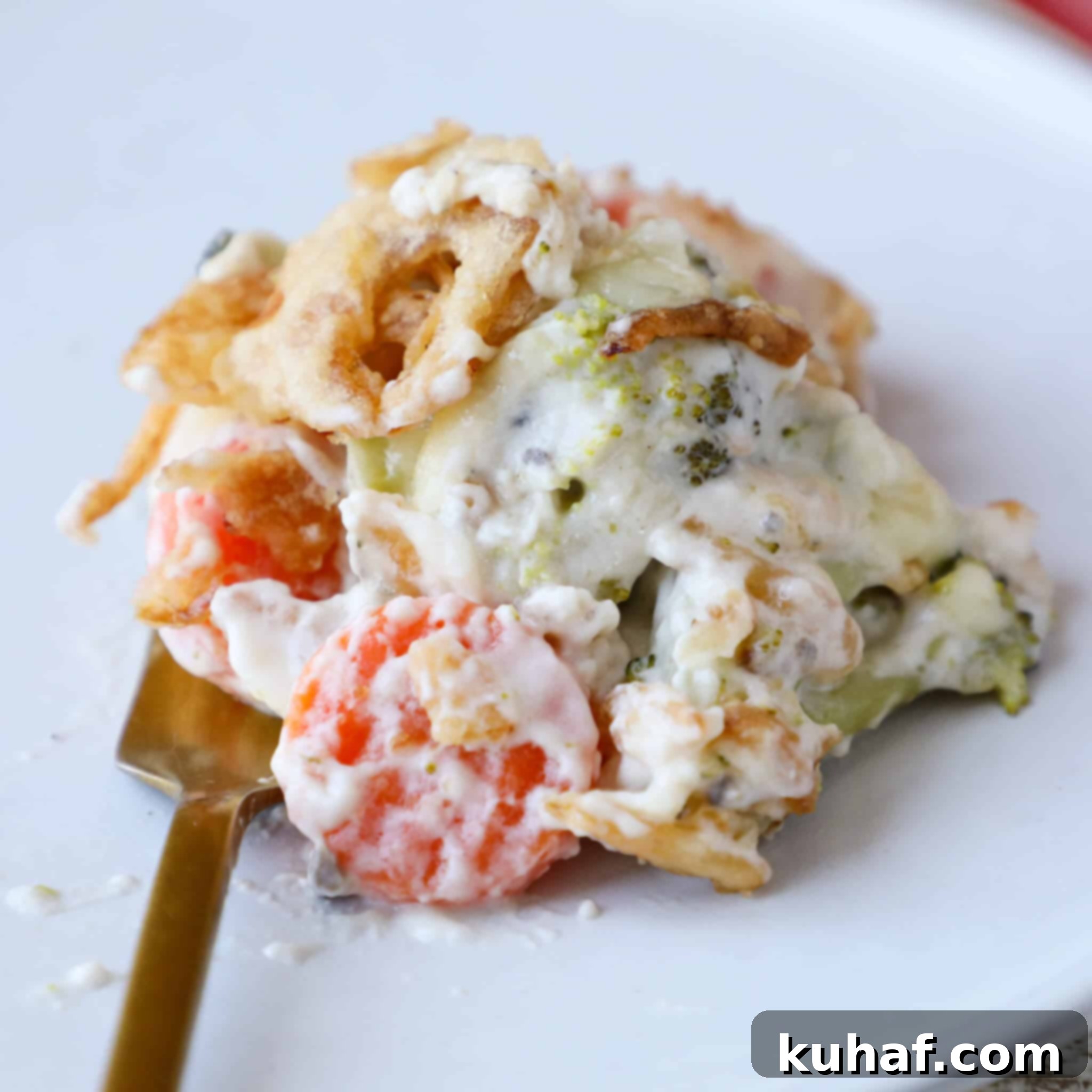Garden Harvest Casserole 3 A generous serving of the creamy Swiss cheese mixed vegetable casserole, golden and bubbling, resting on a white plate with an elegant gold fork, ready to be enjoyed.