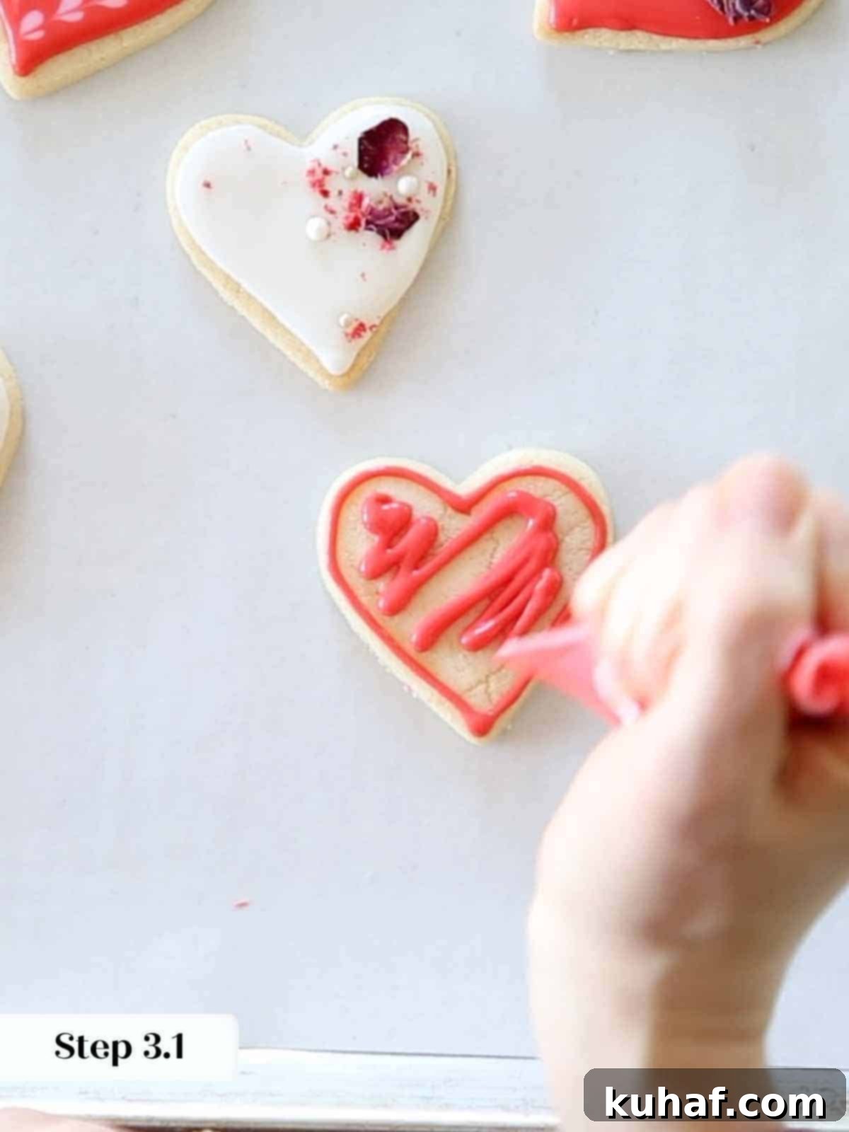 Applying a squiggle of red royal icing inside the outline of a heart cookie, preparing for even spreading and flooding.