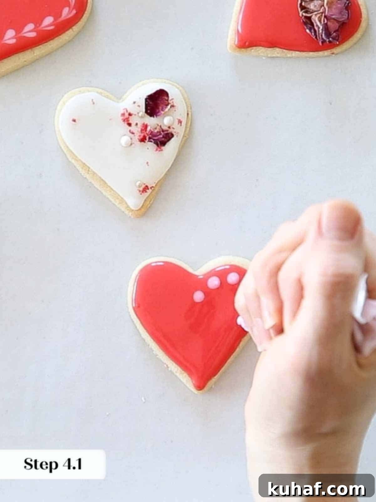 Piping small light pink dots onto wet red royal icing to begin creating a decorative heart pattern.