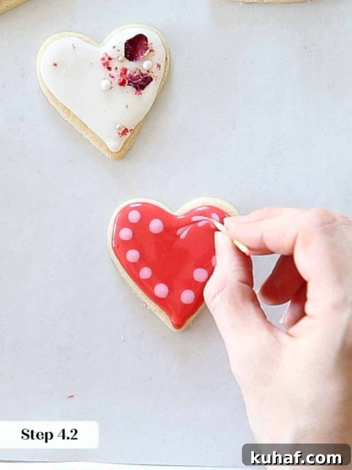 Using a toothpick to drag through wet pink dots on red royal icing, forming the initial shape of tiny hearts.