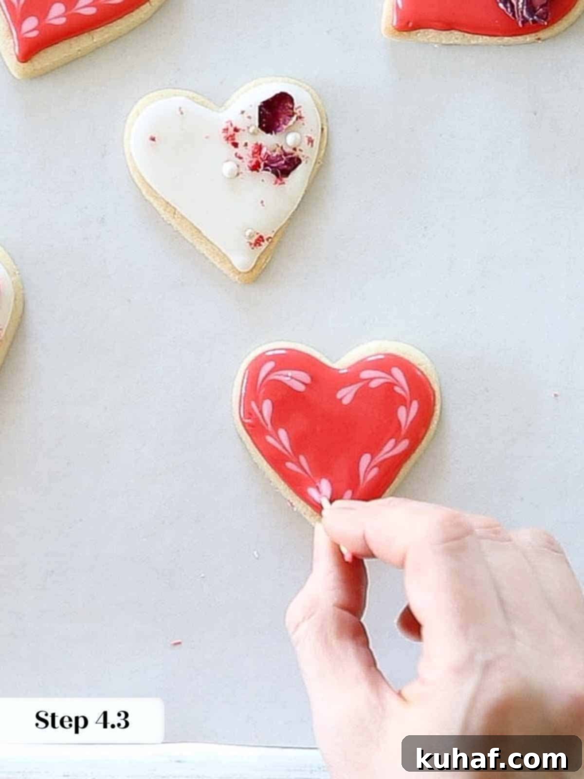 The completed process of creating delicate pink hearts on red royal icing using a toothpick and wet-on-wet technique.