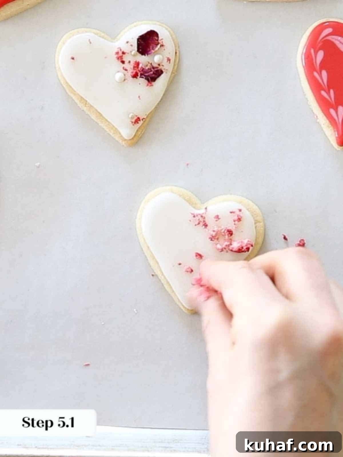 Generously sprinkling crushed dehydrated strawberries onto wet white royal icing on heart cookies for a natural, vibrant topping.
