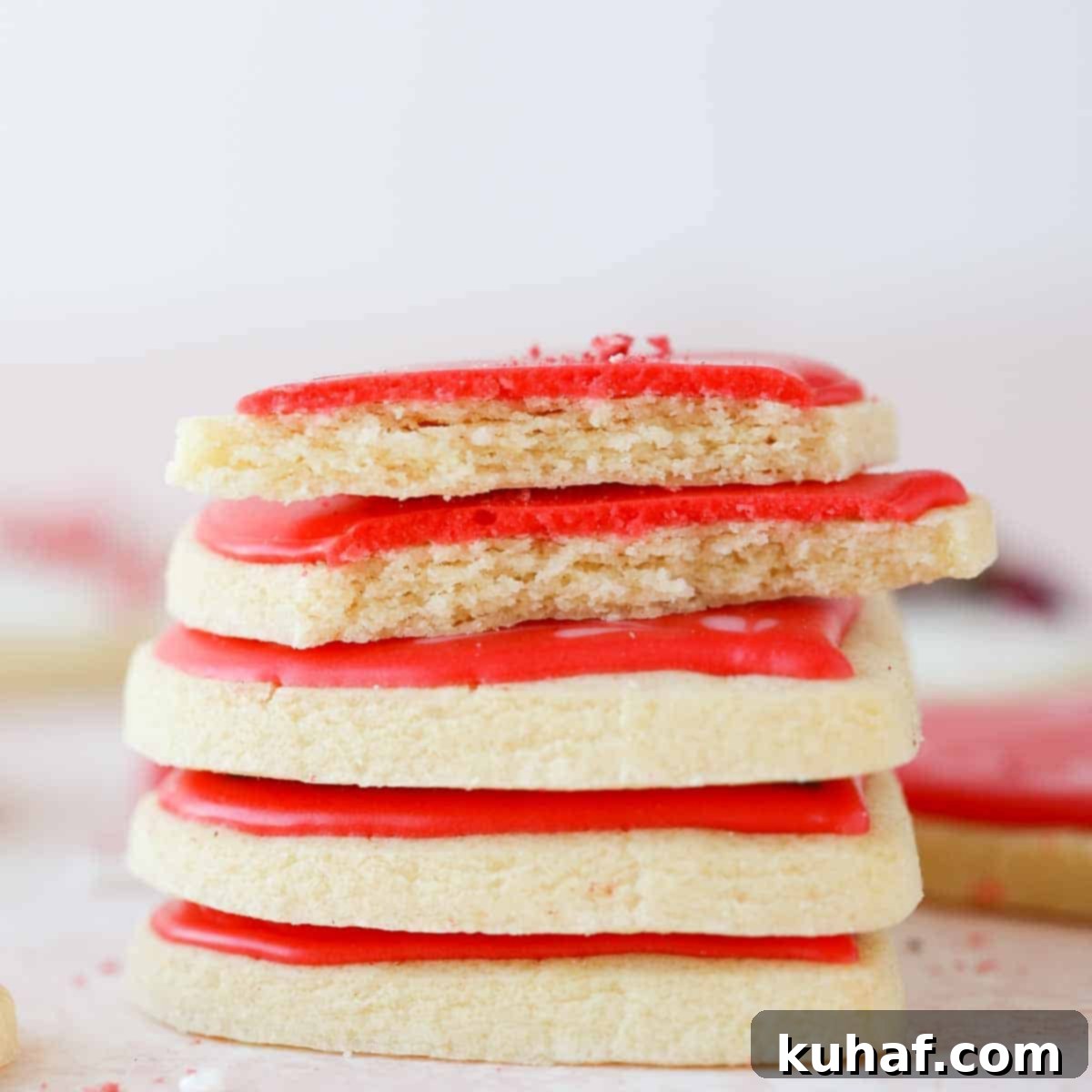 A stack of perfectly iced sugar cookies, some broken open to reveal their soft, chewy interior, highlighting the delicious texture.