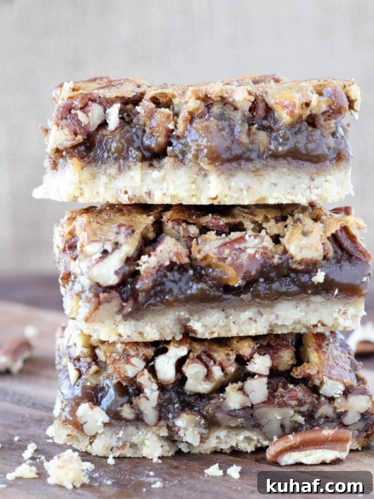 Three golden brown pecan pie bars, stacked neatly, showcasing the rich filling and crumbly crust. A perfect, inviting dessert.
